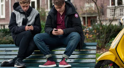 Teenagers using their smartphones on a bench in Amsterdam