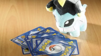 Stock image of a stack of Pokemon cards next to a Vaporeon stuffed animal
