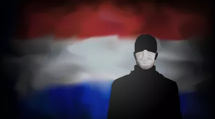 A person in a medical mask in front of the Dutch flag