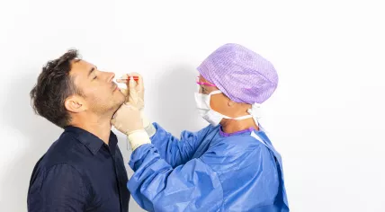 Doctor in protective gear taking a nasal swab from a man