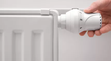 A hand adjusts the temperature on a radiator.