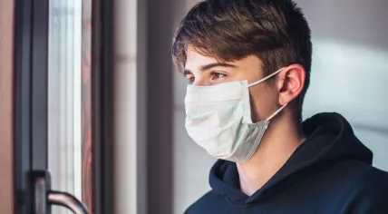 A guy wearing a face mask self-isolating at home.