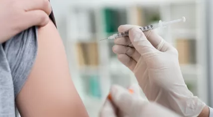 Cropped view of doctor in latex gloves holding syringe and vaccine on blurred foreground near patient