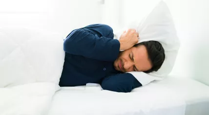Man covering his ears with a pillow.