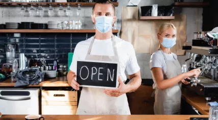 Barista with masks holds open sign