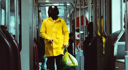 A person in a yellow coat wearing a black face mask in a tram in The Hague. October 2020