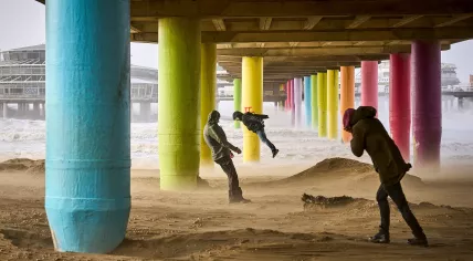 People walk against the wind under a pier on the beach of Scheveningen during Storm Eunice.