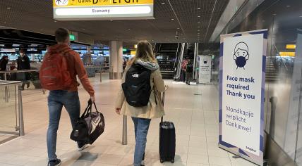 Airline passengers walk past a sign reminding people to wear a face mask at Schiphol Airport. 24 March 2022