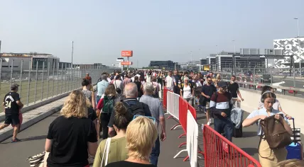 Passengers at Schiphol line up under the sun on a hot afternoon. 18 June 2022