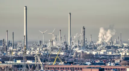 Wind turbines seen through the smoke and chimneys of oil refinery Pernis in Rotterdam