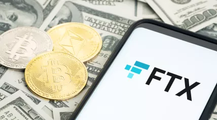 The logo of cryptocurrency exchange FTX, along with coins representing bitcoin and ether, and a pale of U.S. dollars in cash