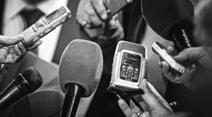 Stock photo of a group of reporters gathered with microphones and audio recorders