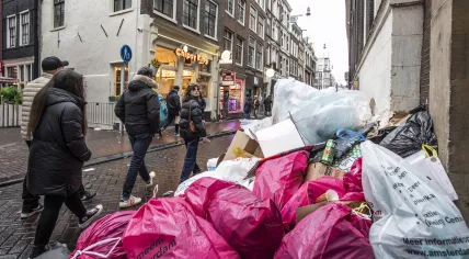 People walk past piled up trash in Amsterdam during a municipal workers' strike, 21 February 2023