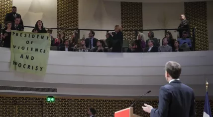 A speech by French President Emmanuel Macron in The Hague is interrupted by several protestors, including one holding a banner reading "President of Violence and Hypocrisy". 11 April 2023