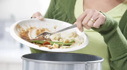 Woman scraping food leftovers into a garbage bin