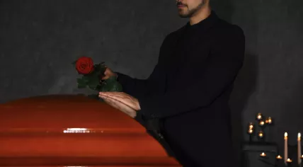 Man putting a red rose on a coffin