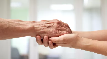 An elderly man's hands are held by a caretaker