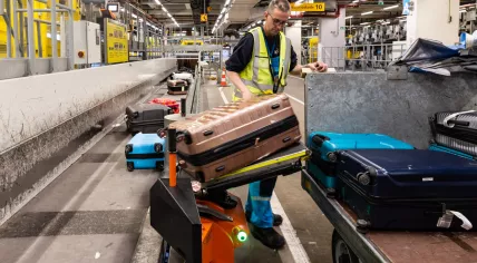 Baggage handler using hoisting equipment to lift a heavy suitcase at Schiphol Airport