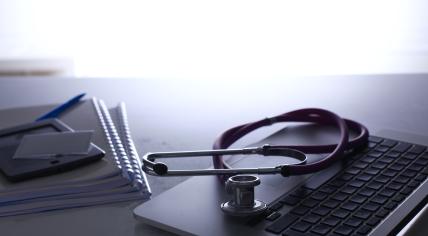 A GP's workspace - a stethoscope on a desk with a laptop and notebooks