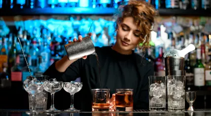 Young female bartender preparing cocktail and carefully pouring it into glass