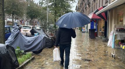 A man with an umbrella walks past covered scooters on a cloudy, rainy day in Amsterdam Oost, 20 October 2023