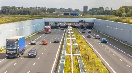 Morning commuting traffic on a4 motorway near The Hague Randstad area. Highway crossing aquaduct tunnel with urban area of Rotterdam in backdrop, Netherlands.