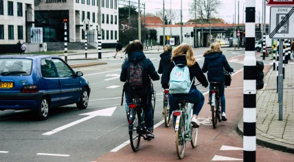 Four cyclists on a bike path passing a car in Voorburg