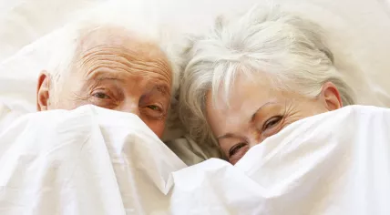An older couple relaxing under the sheets of their bed
