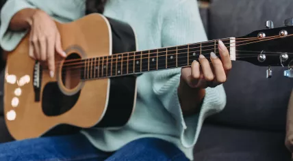 Cropped image of a young woman in turquoise sweater playing acoustic guitar on sofa 
