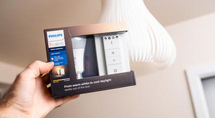 male hand holding the package of new Philips Signify HUE smart light for home with white light luminaire in background