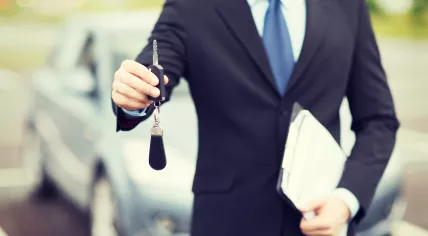 Car rental concept - man in a suit with a car key and clipboard standing in front of a car