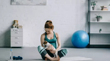 Pregnant woman sitting on yoga mat with jack russell terrier puppy