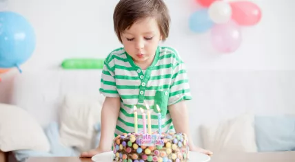 A 4-year-old boy in a green shirt blowing out the candles on his birthday cake
