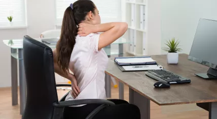 Woman sitting at a desk, stretching her back and neck