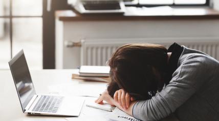 Young tired woman resting her head on her arms at her office desk