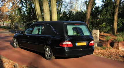 A black hearse at a cemetery in the autumn