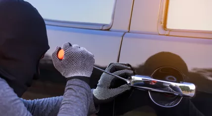 A burglar trying to break into a car with a screwdriver