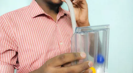A person blowing into a triball incentive Spirometer to test lung capacity