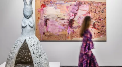 A visitor walks between Leiko Ikemura statue "Baby Hare" and a Martha Jungwirth abstract painting at TEFAF Maastricht in 2023