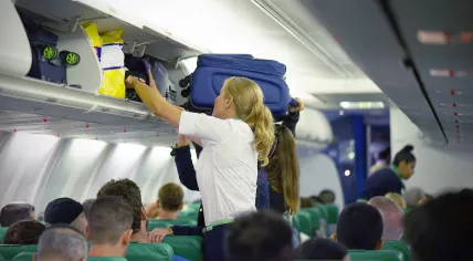 A flight attendant helps a passenger stow carry-on luggage in a plane's overhead compartment