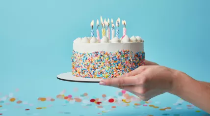 Partial view of birthday cake with candles on blue background with confetti