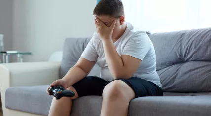 Overweight boy sitting on a coach holding a video game controller