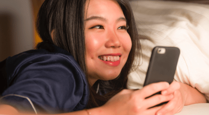 A smiling young woman on a bed holding her phone