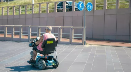 Someone riding a mobility scooter with a cane strapped to the back. 2022