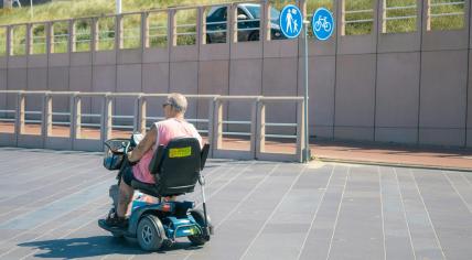 Someone riding a mobility scooter with a cane strapped to the back. 2022