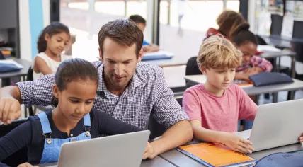 Teacher helping a child on a laptop