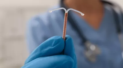 Doctor holding T-shaped intrauterine birth control device on blurred background, closeup