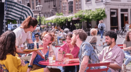 Waitress offering Zilveren Kruis sunscreen to people on a terrace