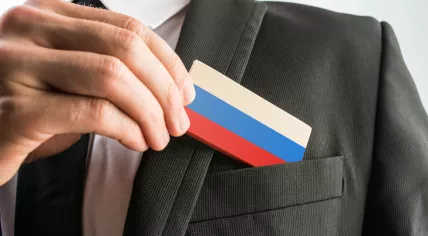 Man pulling a wooden card painted like the Russian flag out of his suit pocket