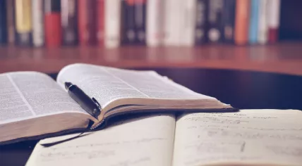 An opened copy of the Bible and an open notebook and pen on a table. 2016